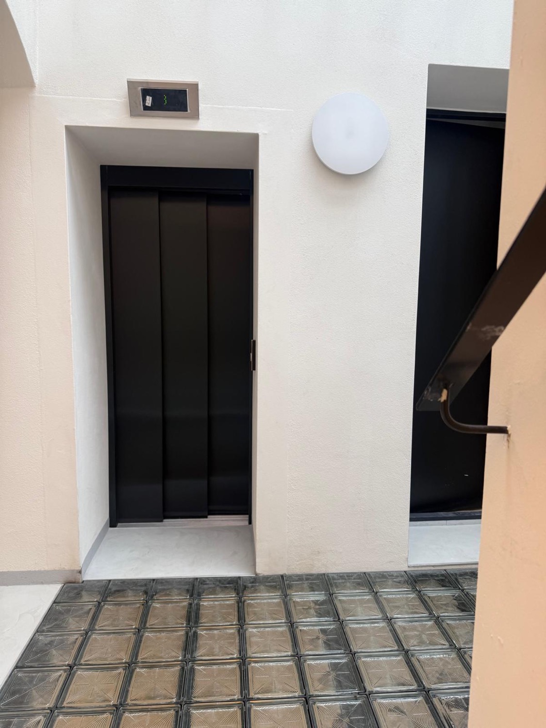 The new lift with black doors, set beside a glass-paved light well